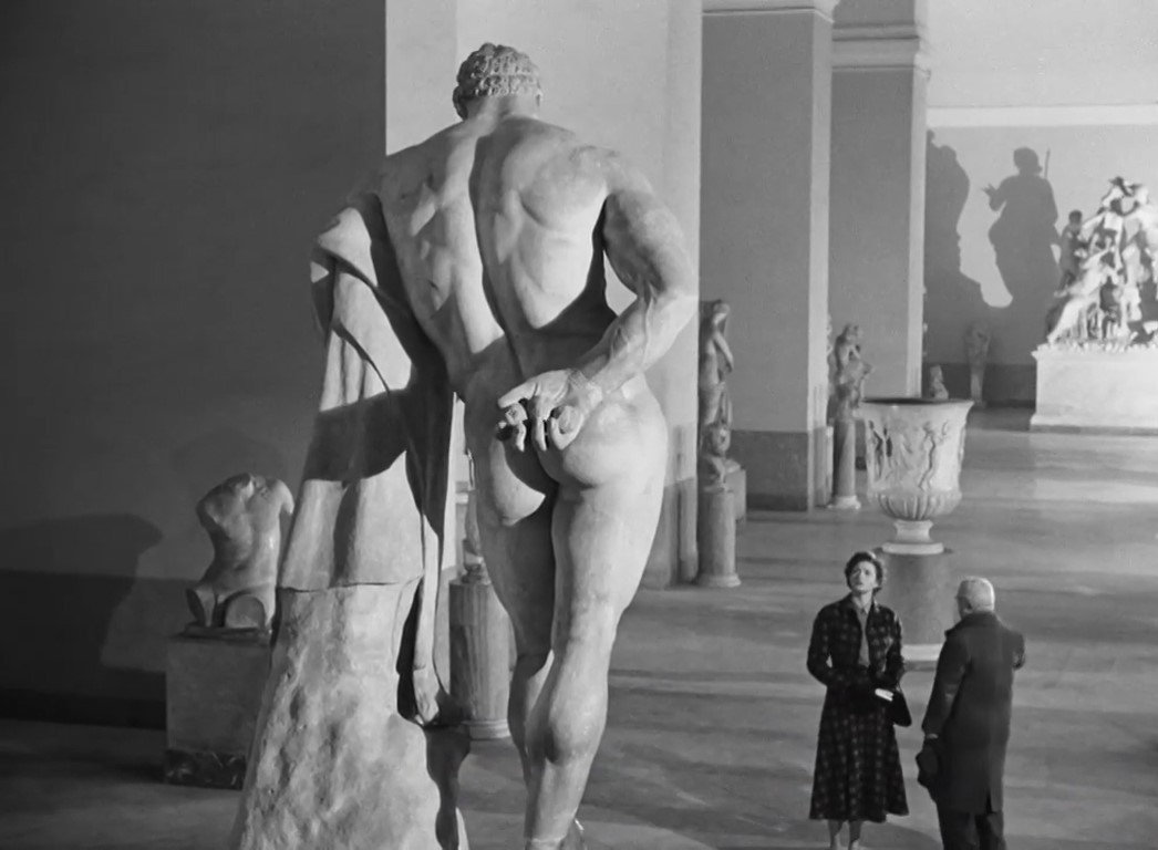 Ingrid mirando con timidez la estatua de Hércules en plano dorsal. 